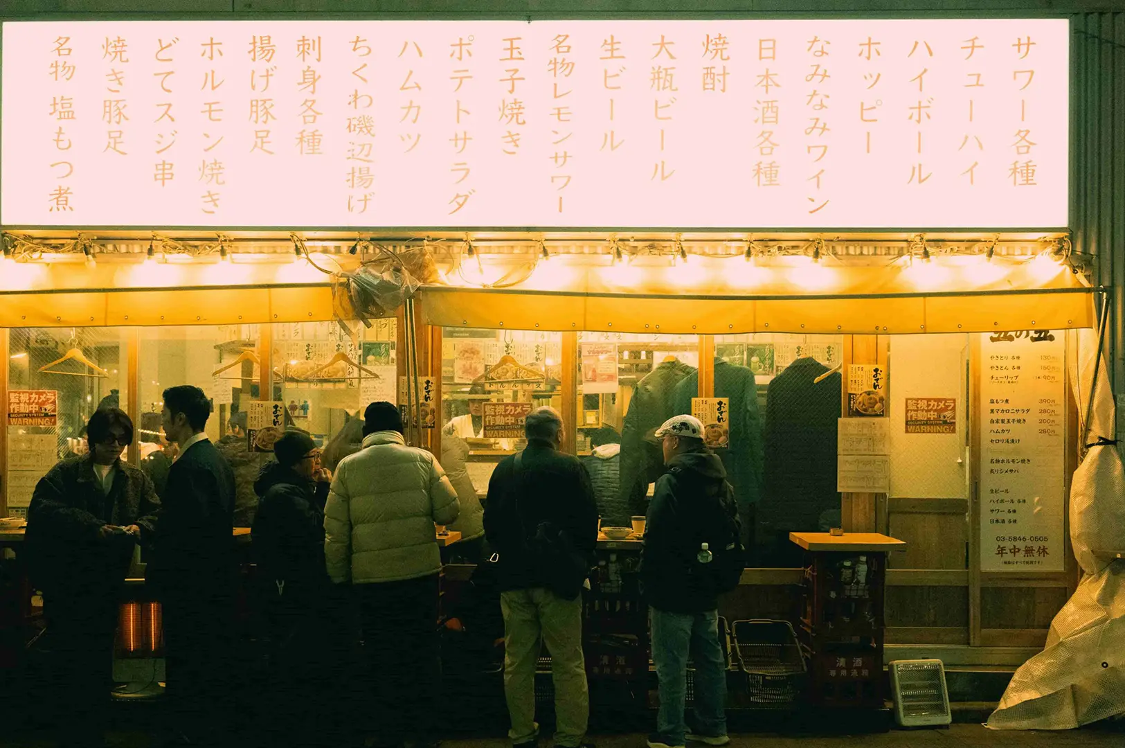 Customers standing outside a traditional Japanese izakaya with a glowing menu sign and warm lighting at night in Singapore