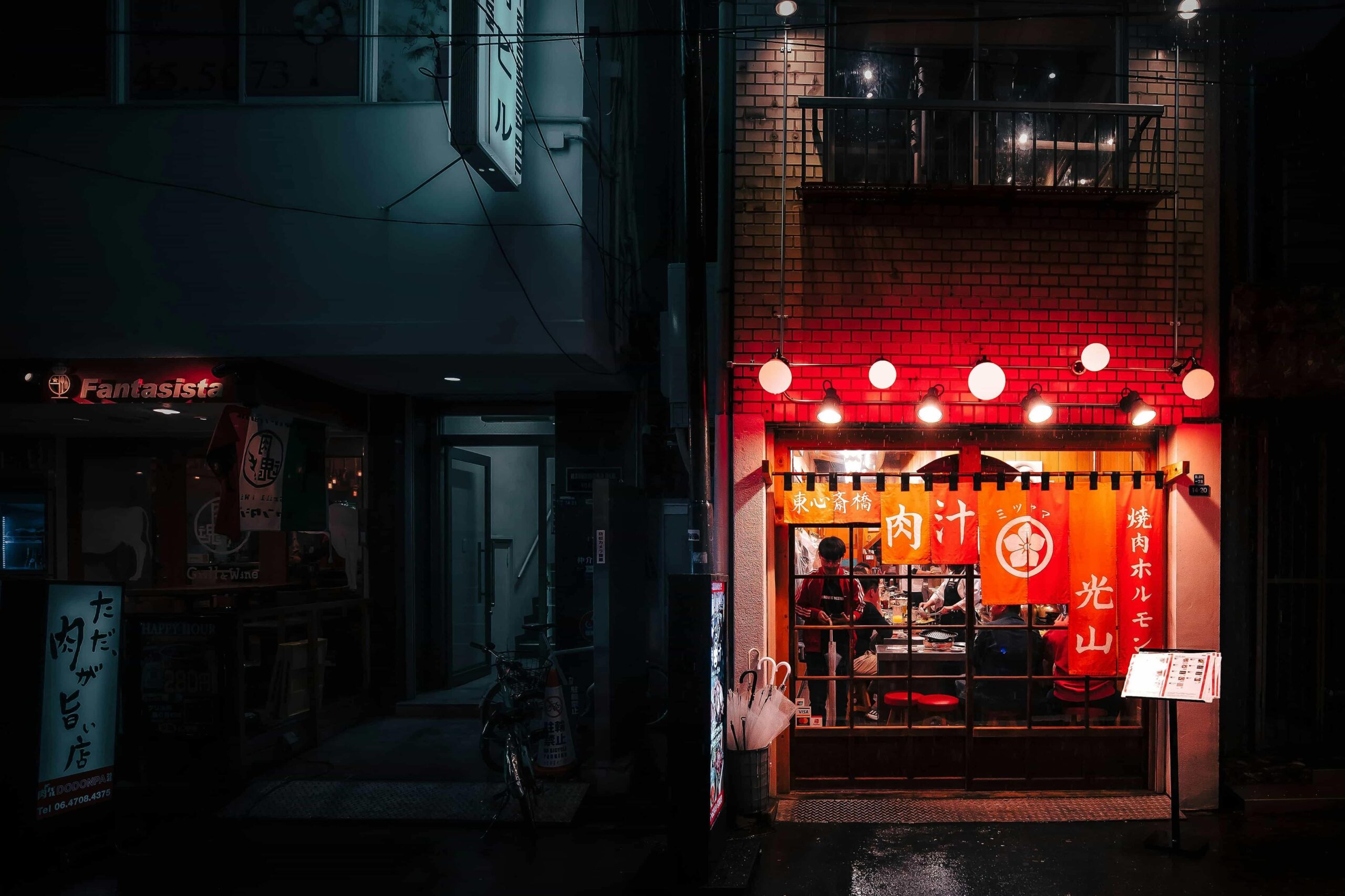 An image of an Izakaya during the late hours, still vibrant by its bright lights and lanterns.
