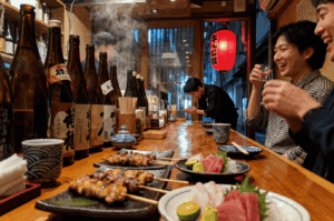 Diners enjoying yakitori, sashimi, and sake at a traditional Japanese izakaya with warm lighting and authentic decor—highlighting communal dining etiquette in Japan’s casual pubs.