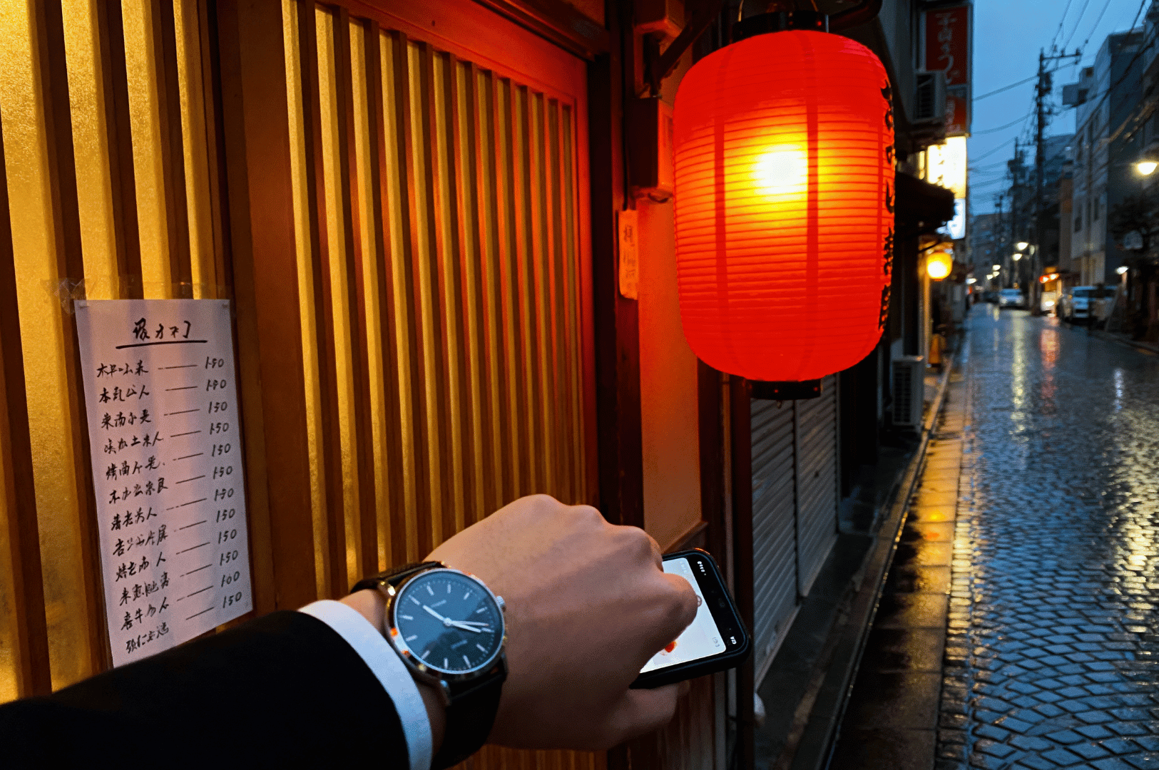 Hand reaching toward a glowing red lantern outside a traditional izakaya on a rainy evening in Japan—highlighting entrance rituals and menu customs in Japanese pub etiquette.