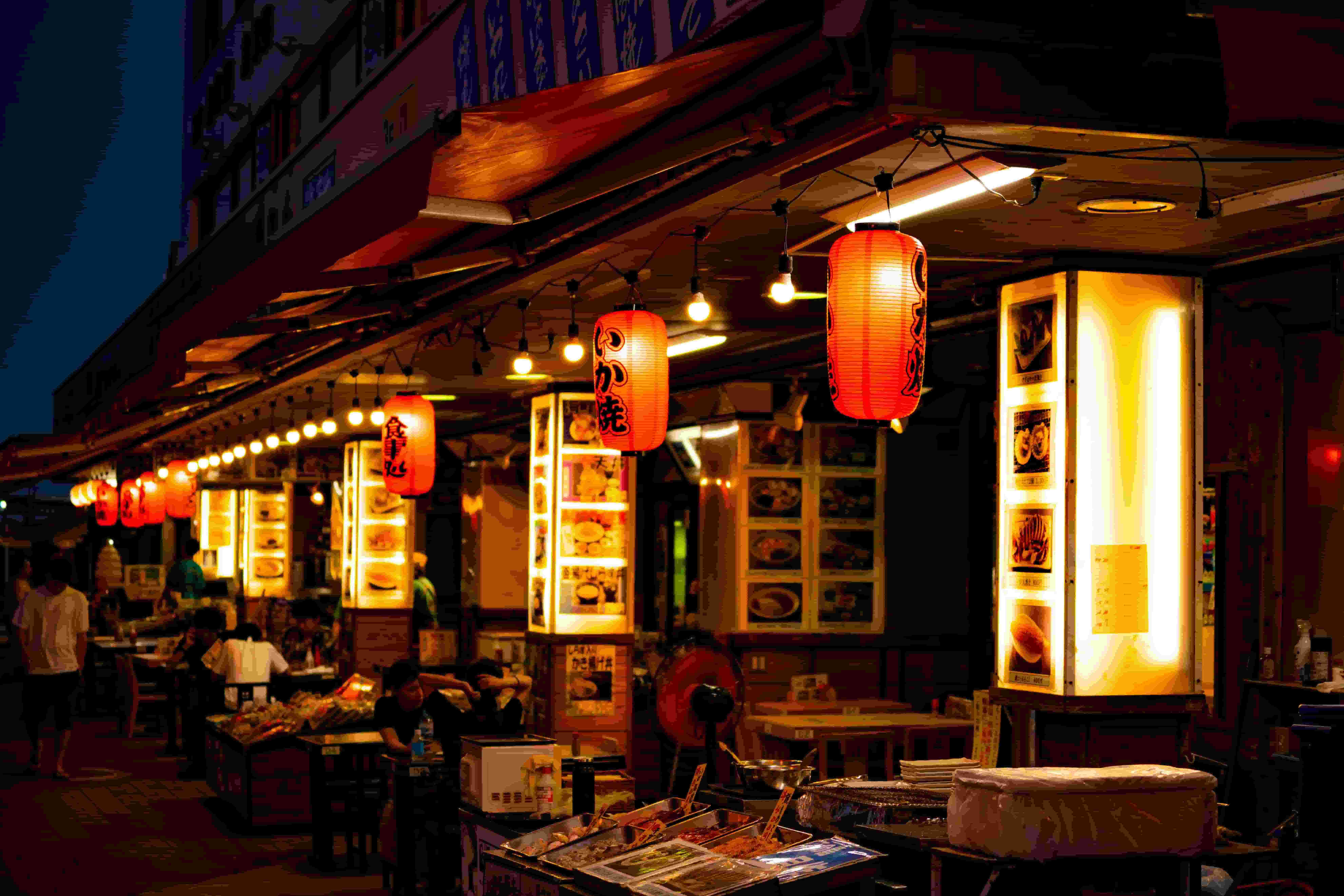 Multiple izakaya stalls standing next to one another as it illuminates in the night with its lanterns and lights.