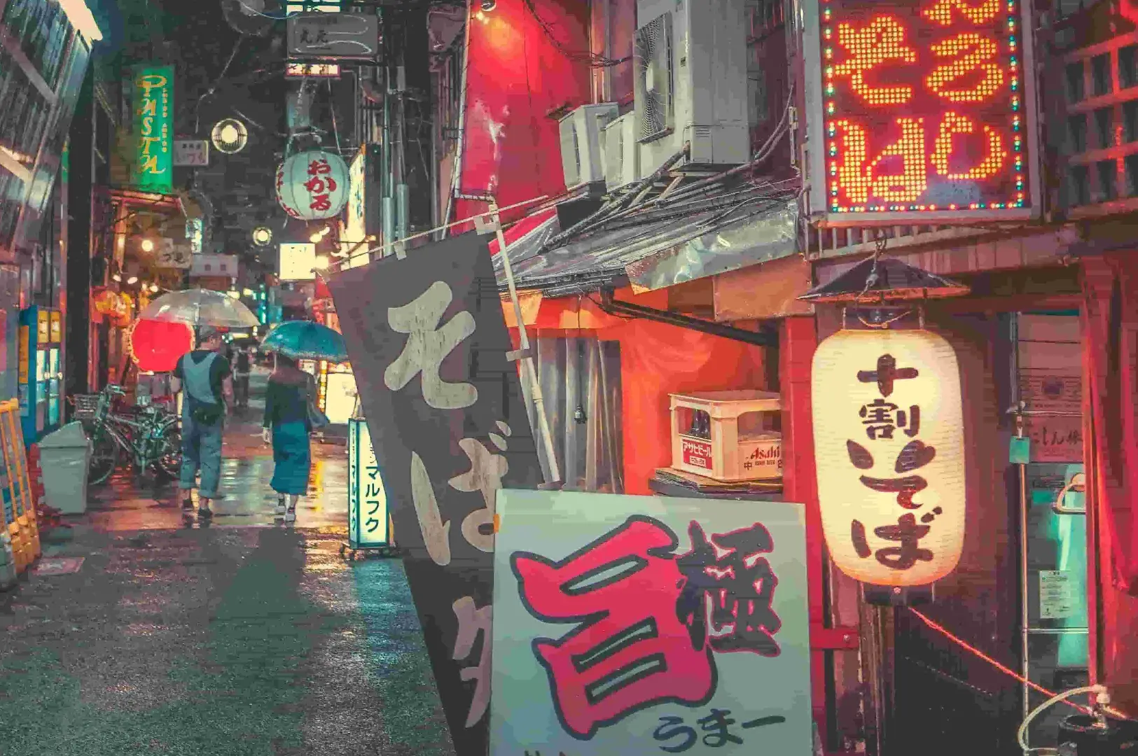 Vibrant, rain-slicked alleyway in Japan at night featuring glowing Japanese lanterns, neon signage, storefront banners, and people walking with umbrellas