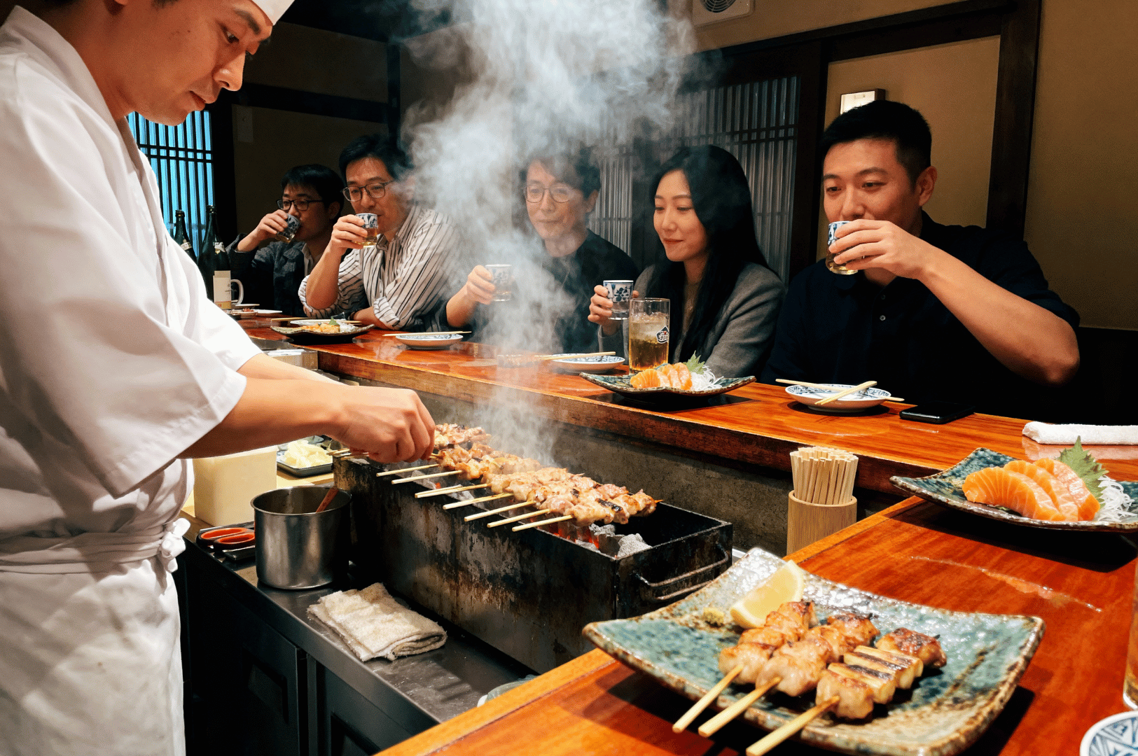 Chef grilling yakitori over charcoal at a Japanese izakaya in Novena, Singapore, with diners enjoying sashimi and drinks at a cozy wooden counter—capturing the authentic rise of Japan-style dining in the city.