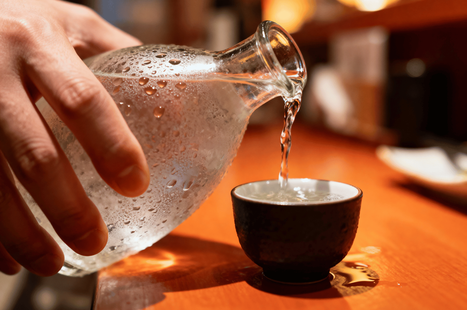 Cold sake being poured from a glass carafe into a ceramic cup at a Japanese izakaya in Novena, Singapore—highlighting the refined drink culture and rising popularity of authentic Japan-style dining in the city.