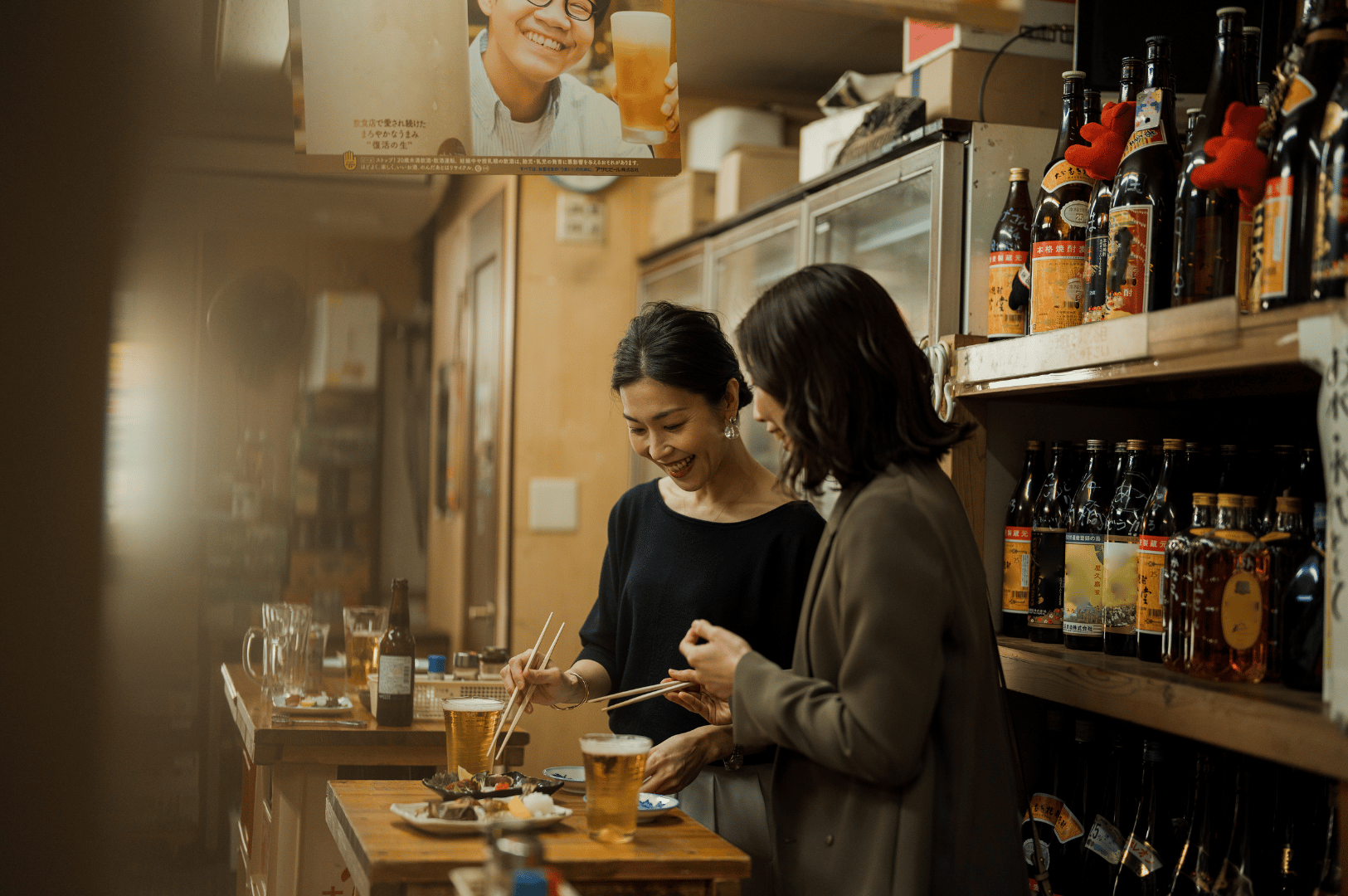 Two guests sharing food and drinks at a cozy Japanese izakaya in Novena, Singapore, surrounded by shelves of liquor and warm lighting—capturing the intimate charm and rising popularity of Japan-style social dining in the city.