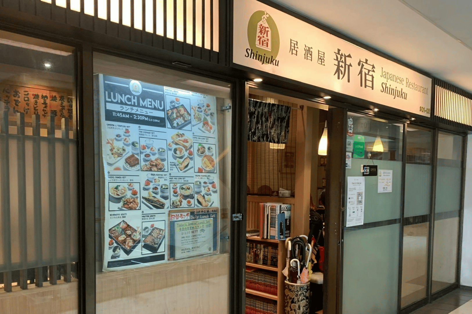 Street-level view of an izakaya called Shinjuku showing lunch menu displays and a welcoming doorway.