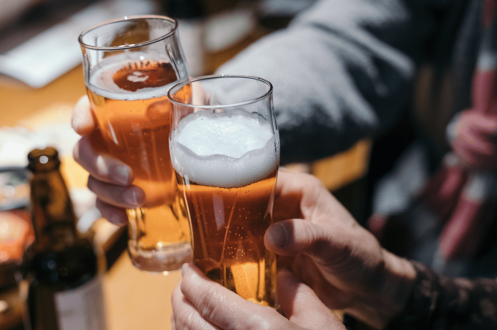 Close-up of two people clinking beer glasses at a cozy izakaya table in Singapore.