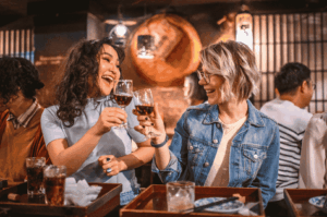 Two friends enjoying seasonal Japanese dishes at a cozy izakaya with warm wooden interiors, celebrating the flavors of Japan’s four seasons over drinks and shared plates.