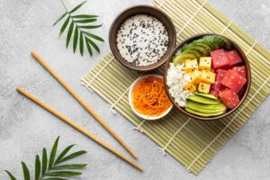 Three bowls of a healthy vegetarian meals laid on a bamboo mat accompanied by decorative stems and chopsticks.