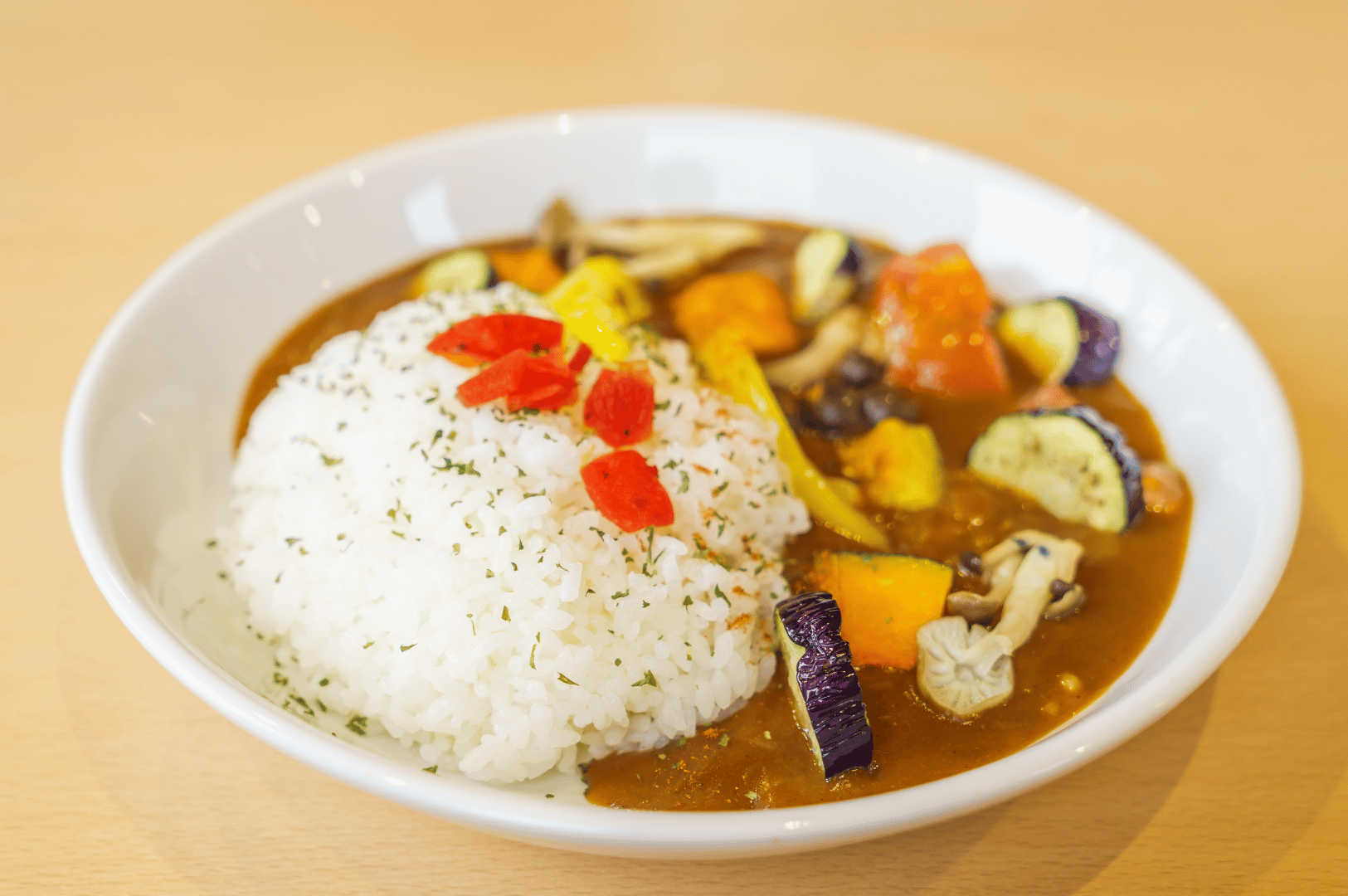 Colorful plate of Japanese vegetable curry with rice, featuring squash, bell peppers, eggplant, and mushrooms in rich brown sauce—showcasing comforting plant-based options at Singapore’s vegetarian izakayas.