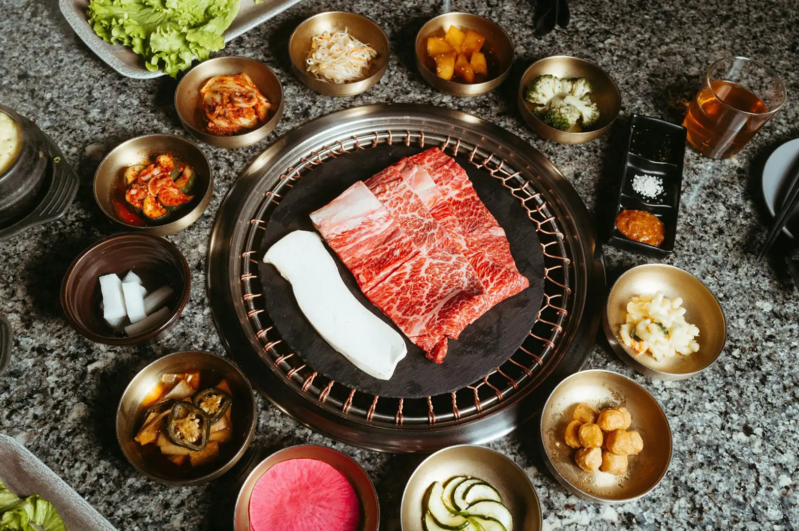 A spread of raw meat, side dishes, and condiments surrounding a tabletop grill at Best Izakaya Singapore