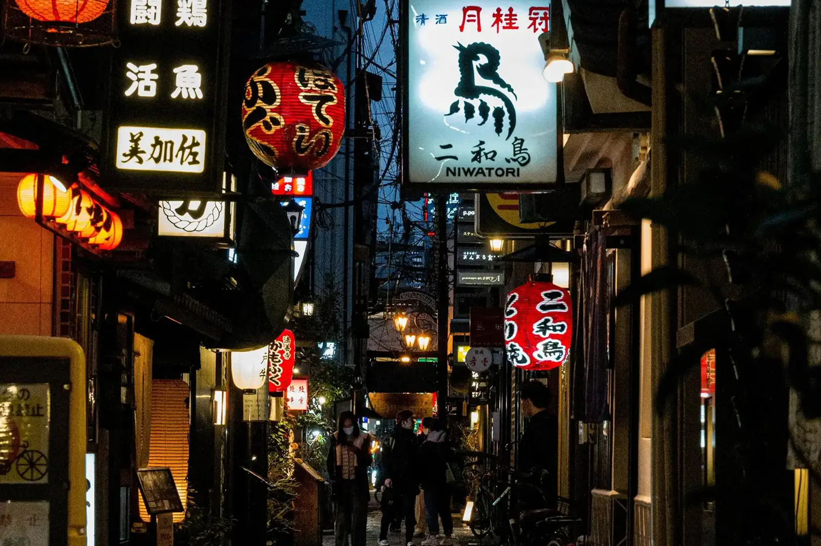 Illuminated Japanese lanterns and glowing neon signs hanging over a narrow alleyway at night at Best Izakaya Singapore