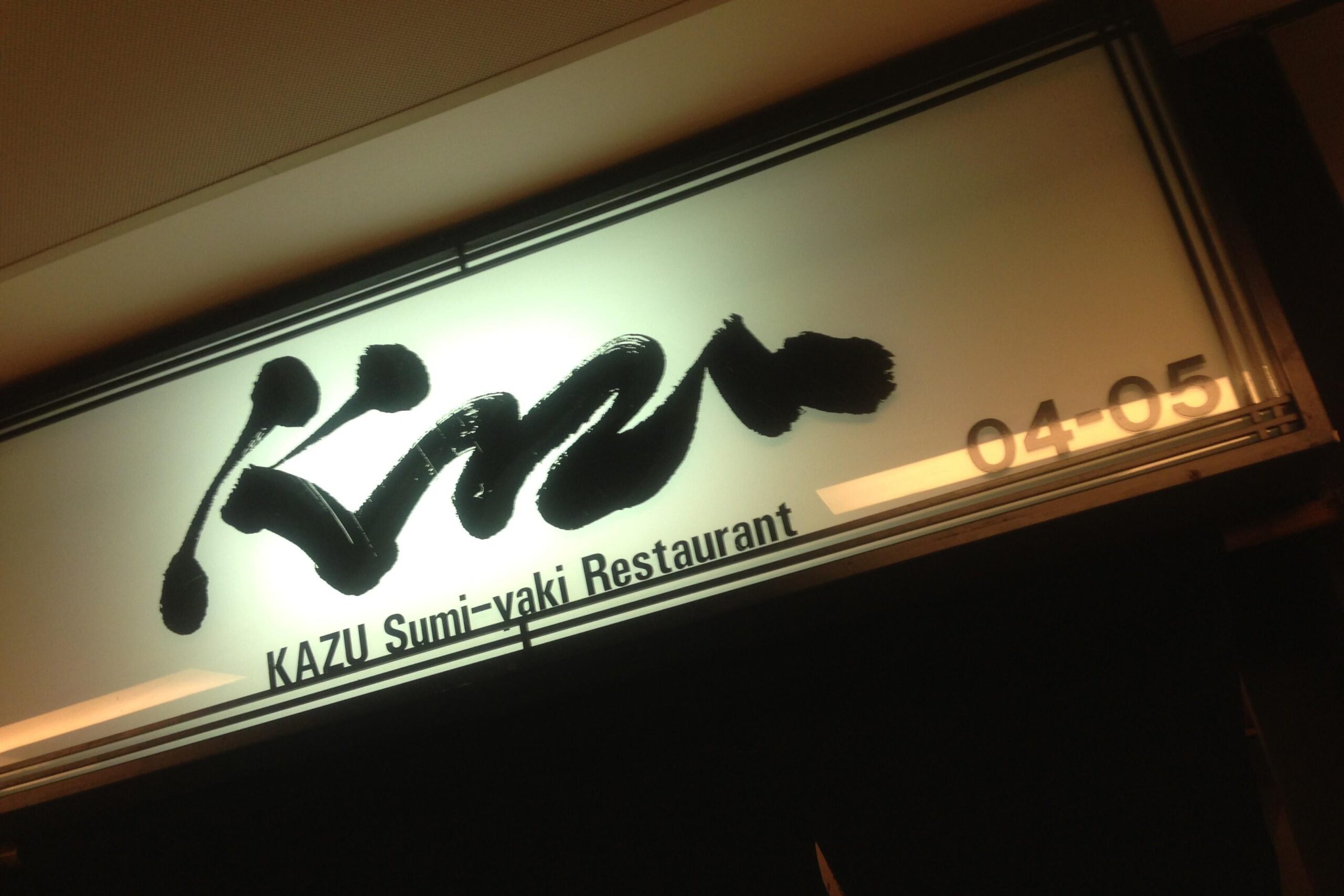 An illuminated rectangular sign features bold, black calligraphic script above the text "KAZU Sumi-yaki Restaurant" and the unit number "04-05."