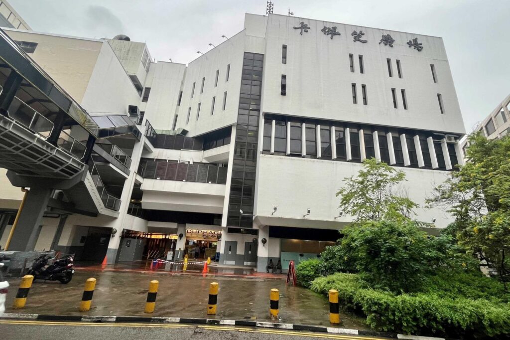 The exterior of Cuppage Plaza is a white, multi-story building featuring a covered walkway, prominent signage in both Chinese characters and English, and a paved entrance area.