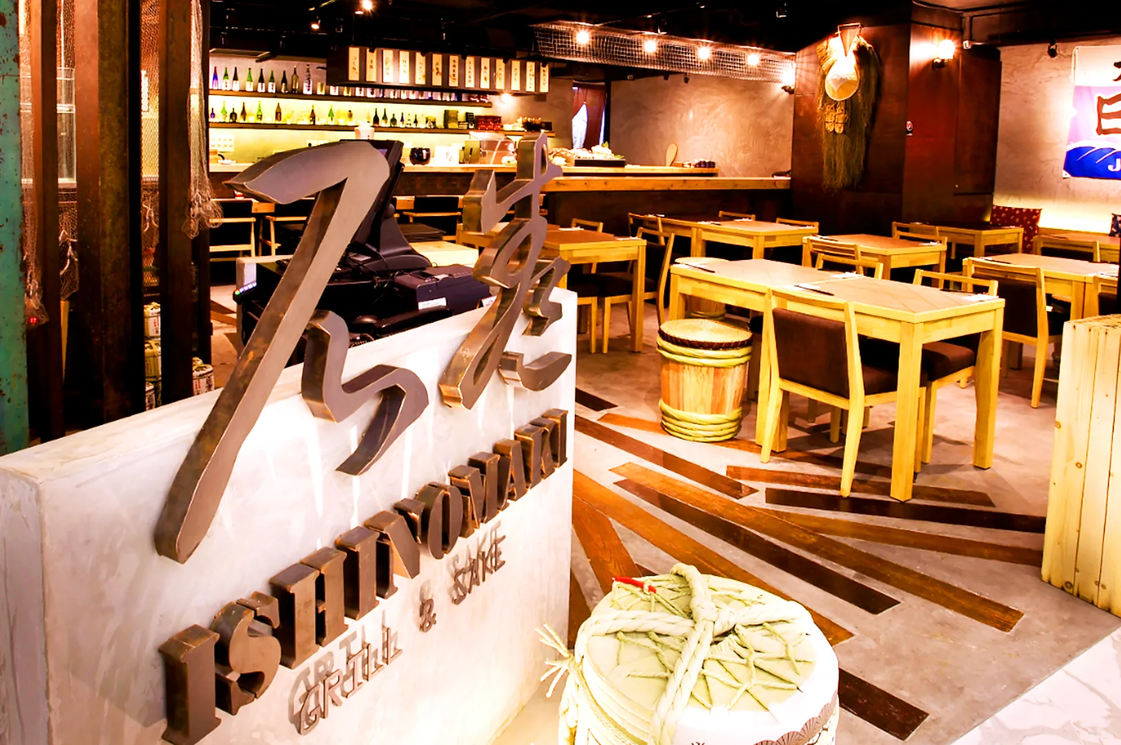 Modern izakaya interior at Ishinomaki Grill & Sake Singapore with wooden tables, sake barrels, and warm ambient lighting near Orchard Road