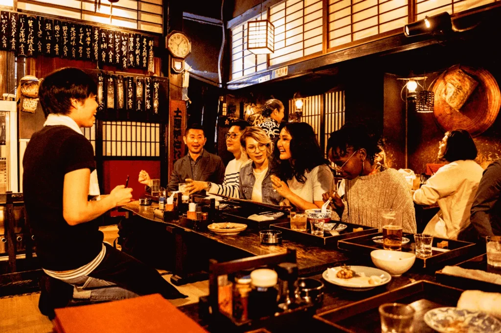 Singapore izakaya interior with diners enjoying yakitori skewers and drinks, warm lighting casual Japanese dining atmosphere shared table experience