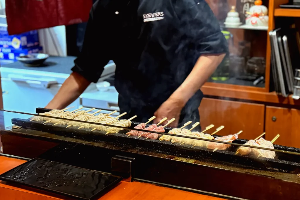Chef grilling assorted yakitori skewers at Japanese izakaya counter