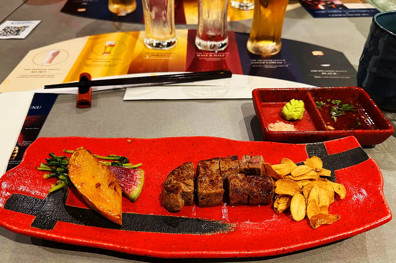 Premium grilled beef steak platter with garlic chips and wasabi served at Singapore izakaya with beer tasting set in the background