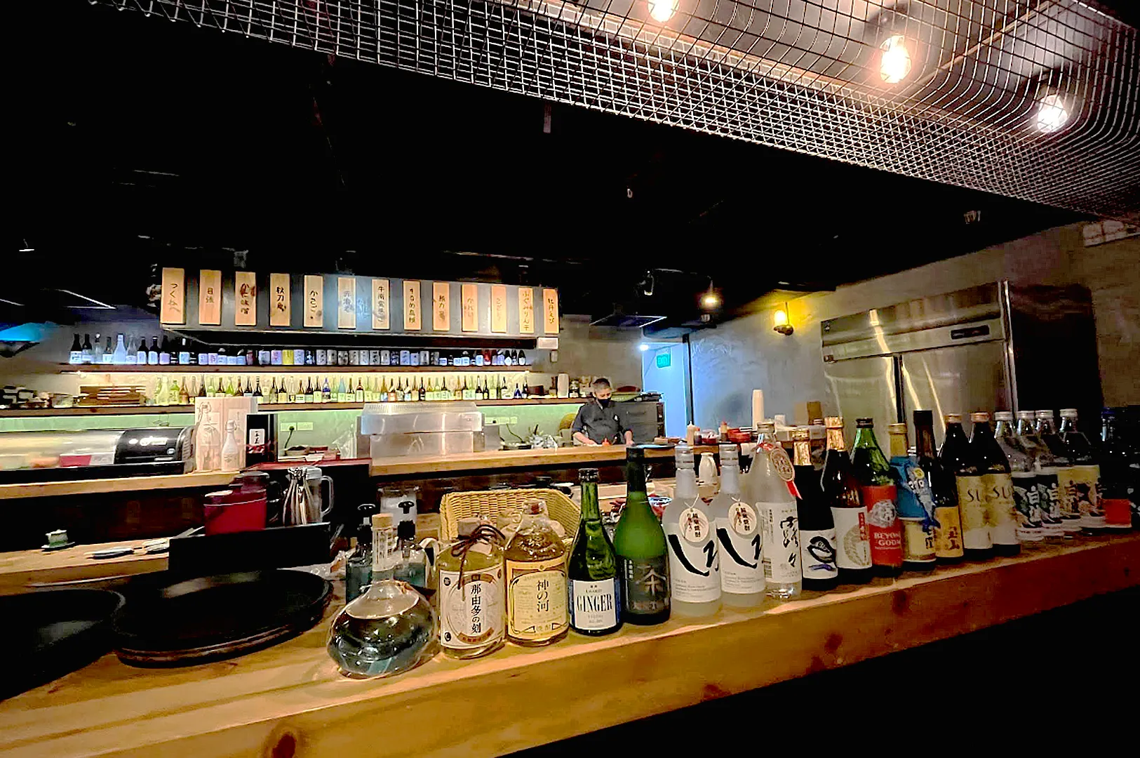 Wide selection of Japanese sake bottles displayed at izakaya bar counter in Singapore with open kitchen dining experience