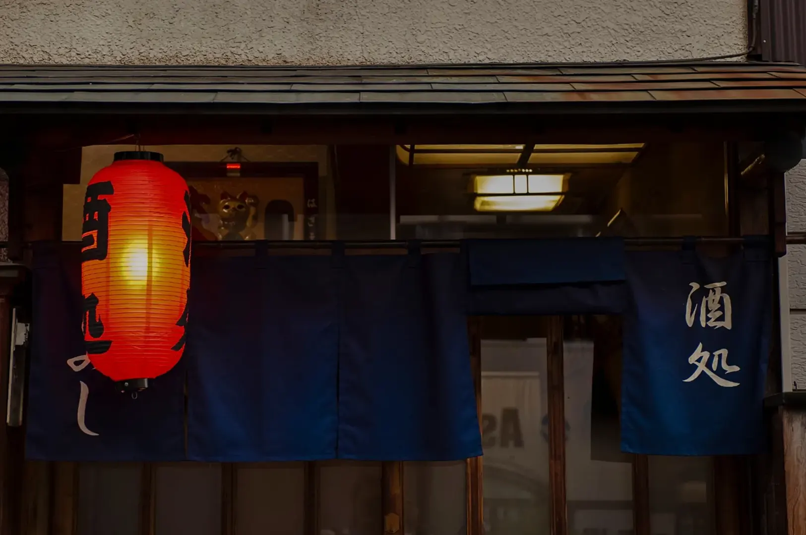 Red lantern and blue noren curtain at izakaya entrance.