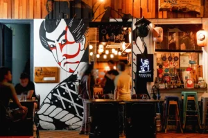 Japanese izakaya exterior in Singapore with traditional mural art, lantern lighting, and outdoor seating at night