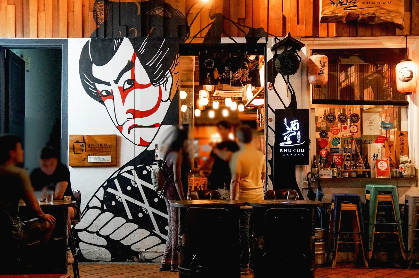 Japanese izakaya exterior in Singapore with traditional mural art, lantern lighting, and outdoor seating at night