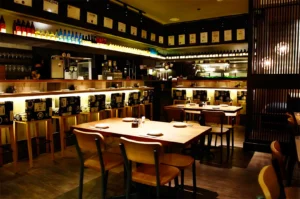 Cozy modern izakaya interior in Singapore with wooden tables, sake bottle display, warm ambient lighting, and Japanese bar seating