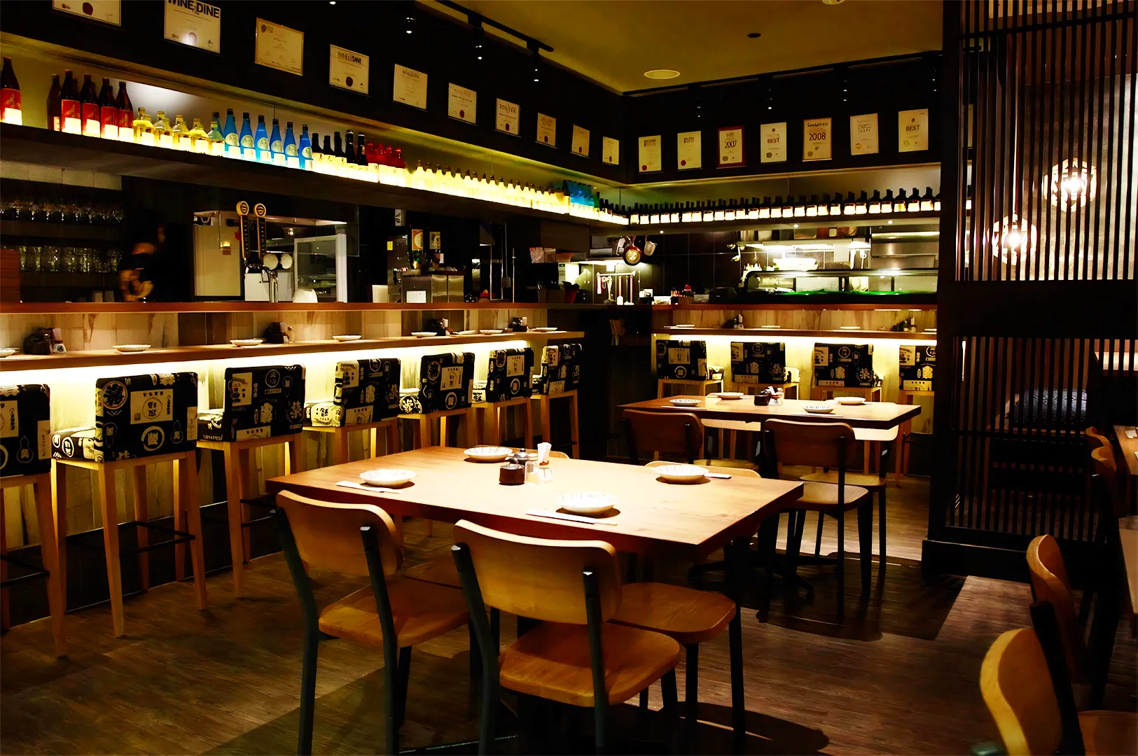 Cozy modern izakaya interior in Singapore with wooden tables, sake bottle display, warm ambient lighting, and Japanese bar seating