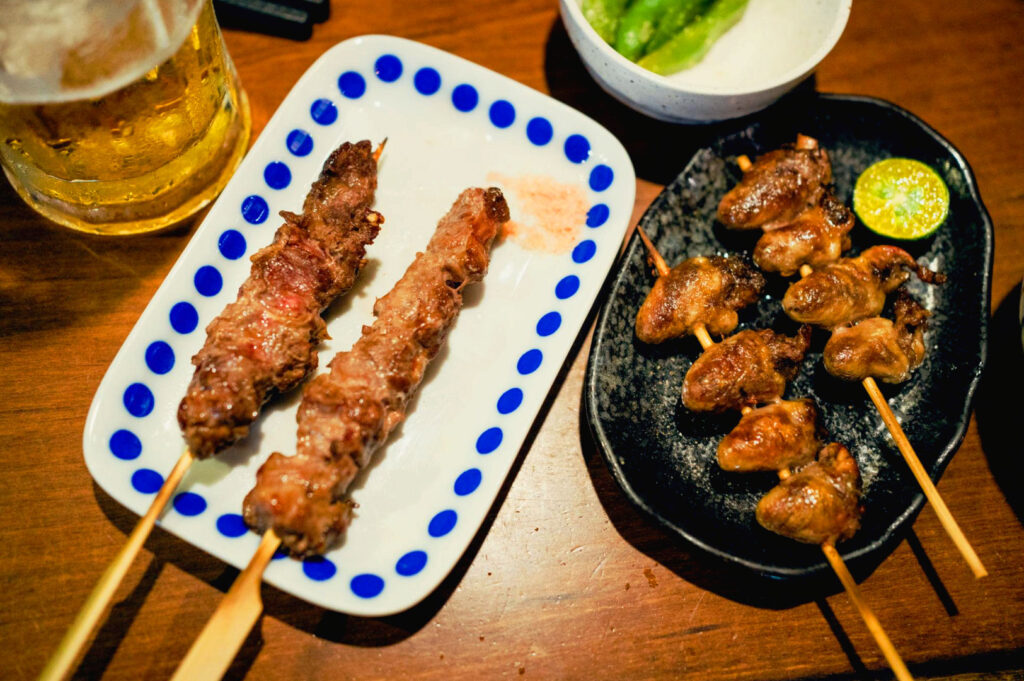 Japanese yakitori skewers and cold beer served at a cozy izakaya table, featuring grilled chicken skewers, charcoal flavors, and casual late-night dining vibes.