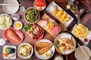 Overhead view of a crowded izakaya table filled with yakitori skewers, sashimi, karaage, tamagoyaki, grilled fish, edamame, and Japanese sharing dishes on small plates