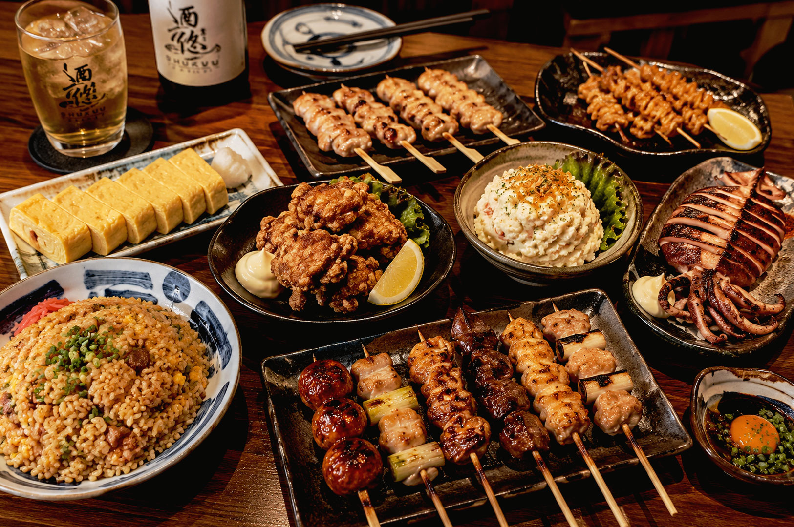 Assorted yakitori skewers, Japanese fried rice, grilled squid, tamagoyaki, and karaage served on small plates at a warm izakaya dining table in Singapore