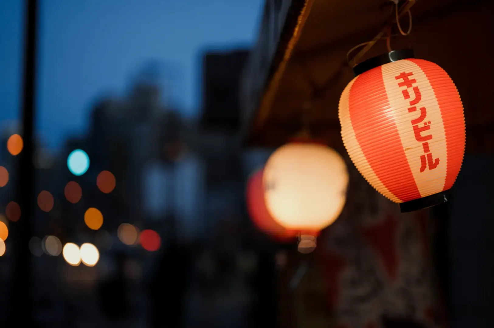 Red paper lanterns at dusk with bokeh lights.