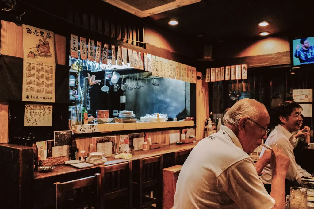 Izakaya counter with diners, warm lighting, and kitchen visible through service window.