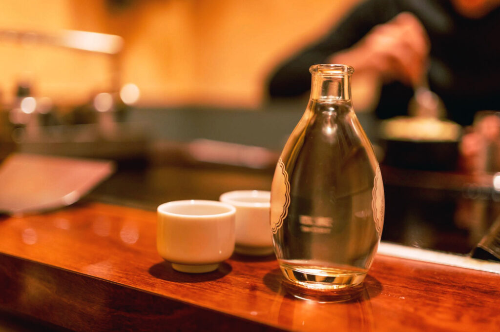 Warm Japanese izakaya sake set with ceramic cups on a wooden counter in , capturing the quiet atmosphere of a late-night Japanese dining experience.