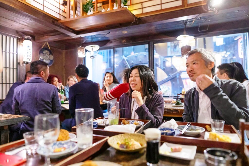 Group of diners enjoying food and drinks inside a busy Japanese izakaya restaurant with lively atmosphere and shared plates