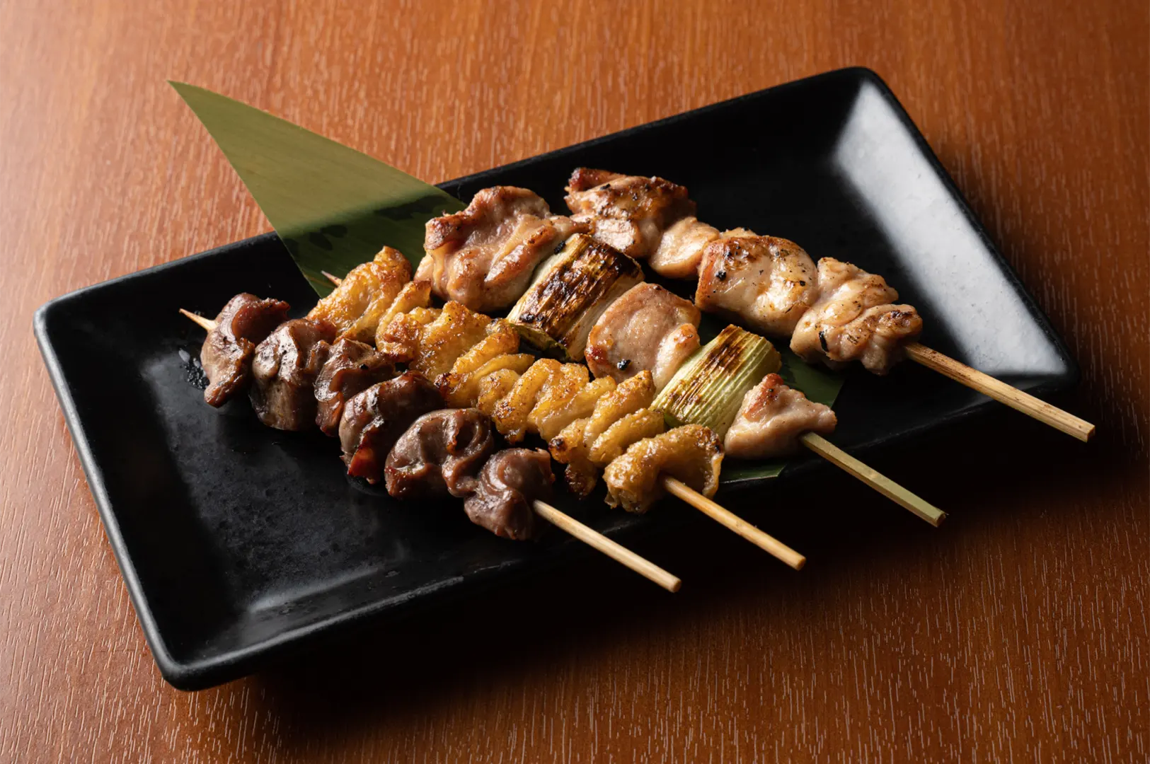 Assorted yakitori skewers on black plate.