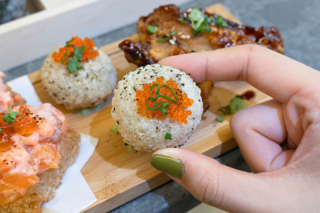 Close-up of crispy Japanese rice ball topped with ikura salmon roe at modern handroll sushi bar
