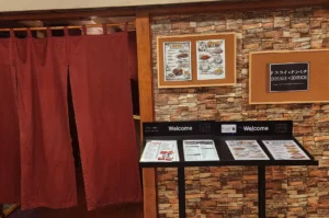 Entrance of Dosukoi x Donpachi with red curtain and menu stands.