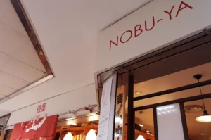 NOBU-YA restaurant exterior with a red noren curtain and signage.