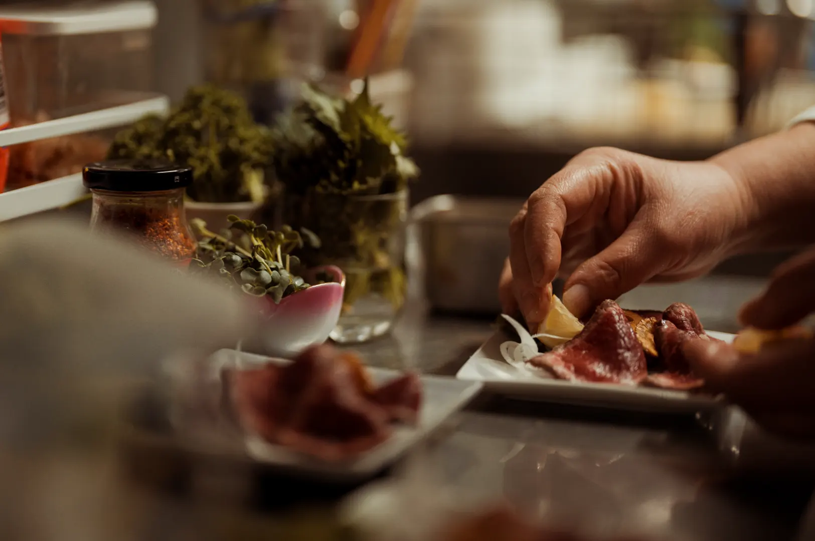 A chef is arranging slices of meat on a white plate and adding lemon wedges.