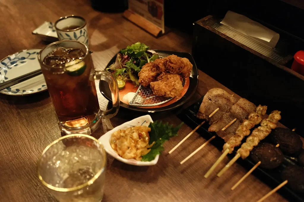 Izakaya table with drinks, karaage, skewers, and small dishes.