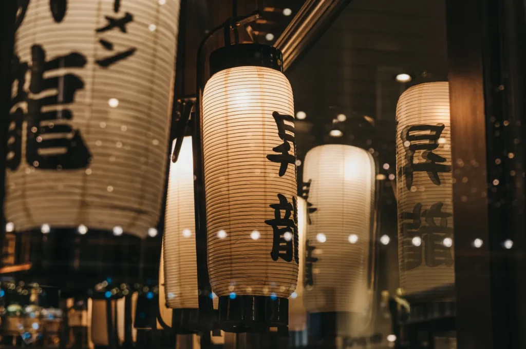 Warm Japanese lanterns with black calligraphy hanging inside a restaurant window.