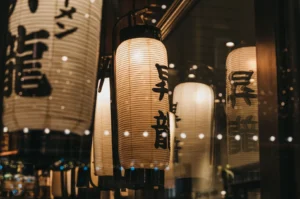 Warm Japanese lanterns with black calligraphy hanging inside a restaurant window.