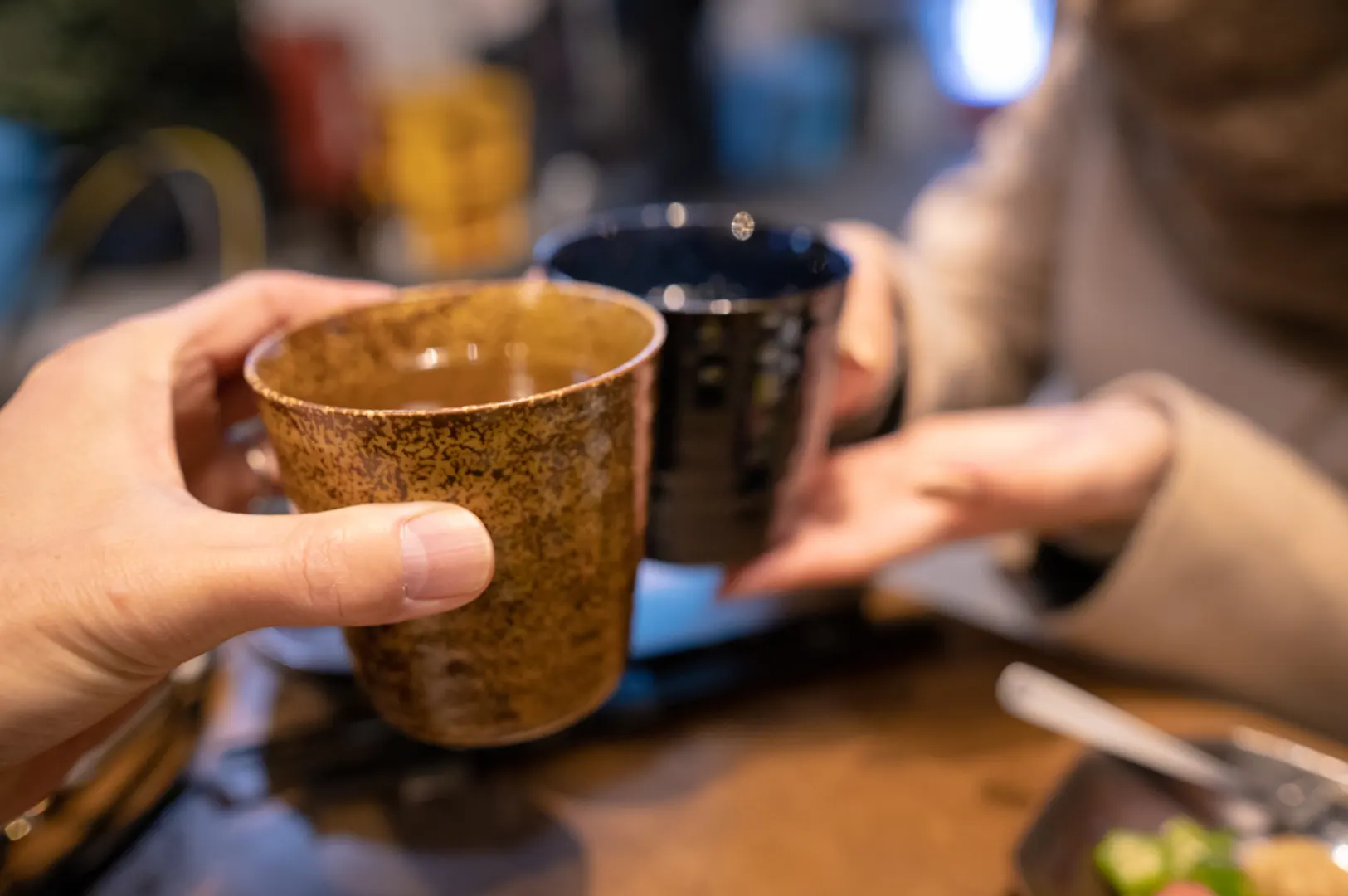 Two hands holding up cups for a toast, with a plate of food in the foreground.