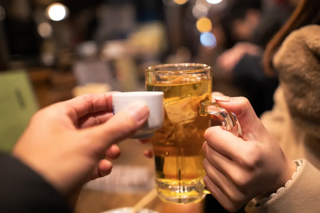 Hands toasting with beer mug and sake cup at izakaya.