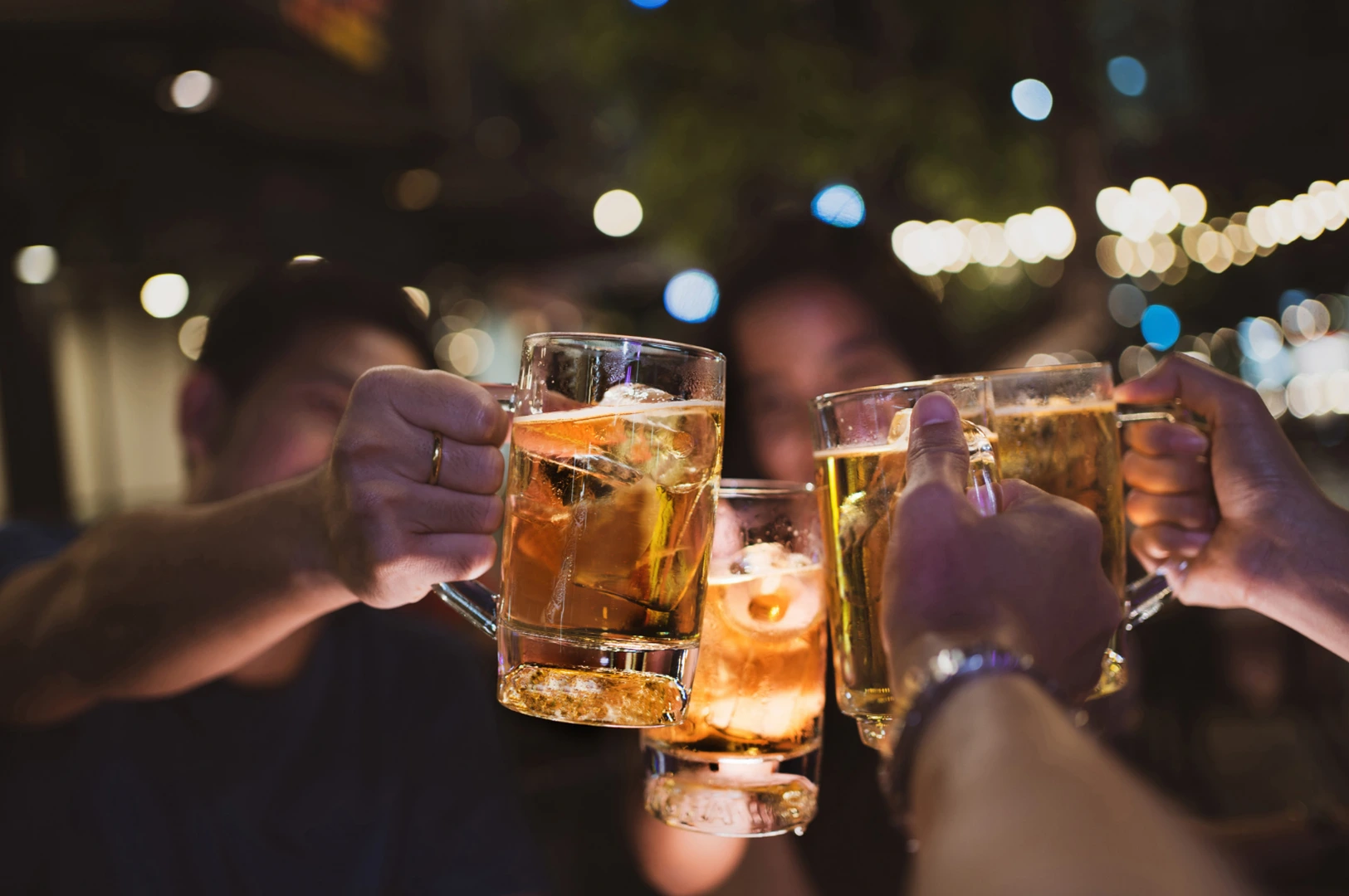 Hands toasting with beer glasses at night.