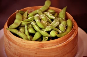 A close-up of steamed edamame pods sprinkled with salt in a bamboo steamer basket.