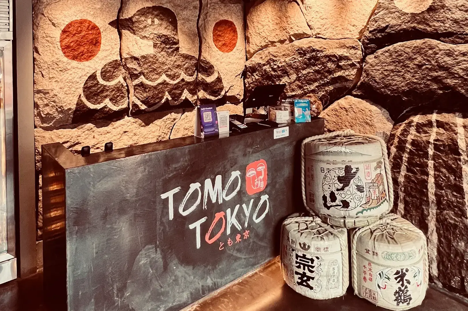 Tomo Tokyo entrance with sake barrels and stone wall with Japanese flag motif.