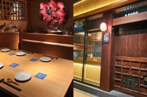 A warmly lit Japanese restaurant entryway with a wooden facade, red lantern, and narrow seating area.