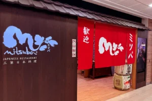 Mitsuba Japanese Restaurant entrance with a red noren curtain, dark wood facade, and Japanese signage.